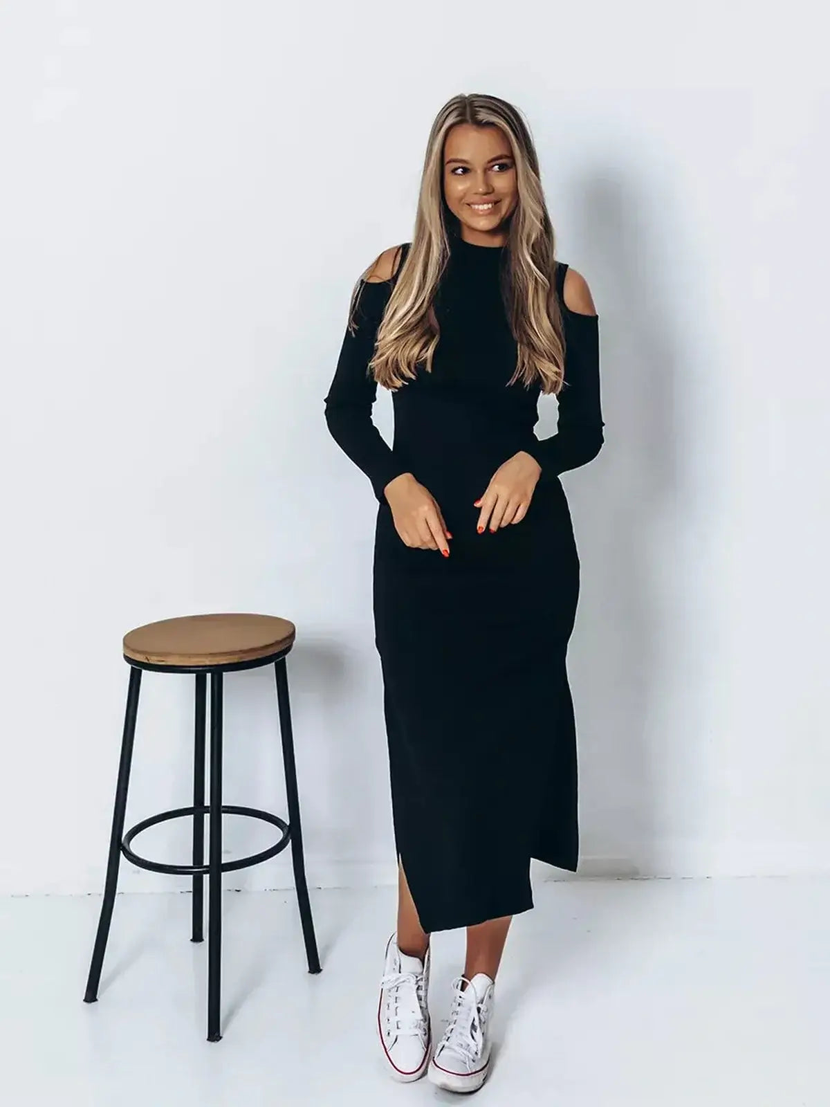 Model wearing a sleek black Shadow Midi Dress with cutout shoulders and side slit, styled with white sneakers.