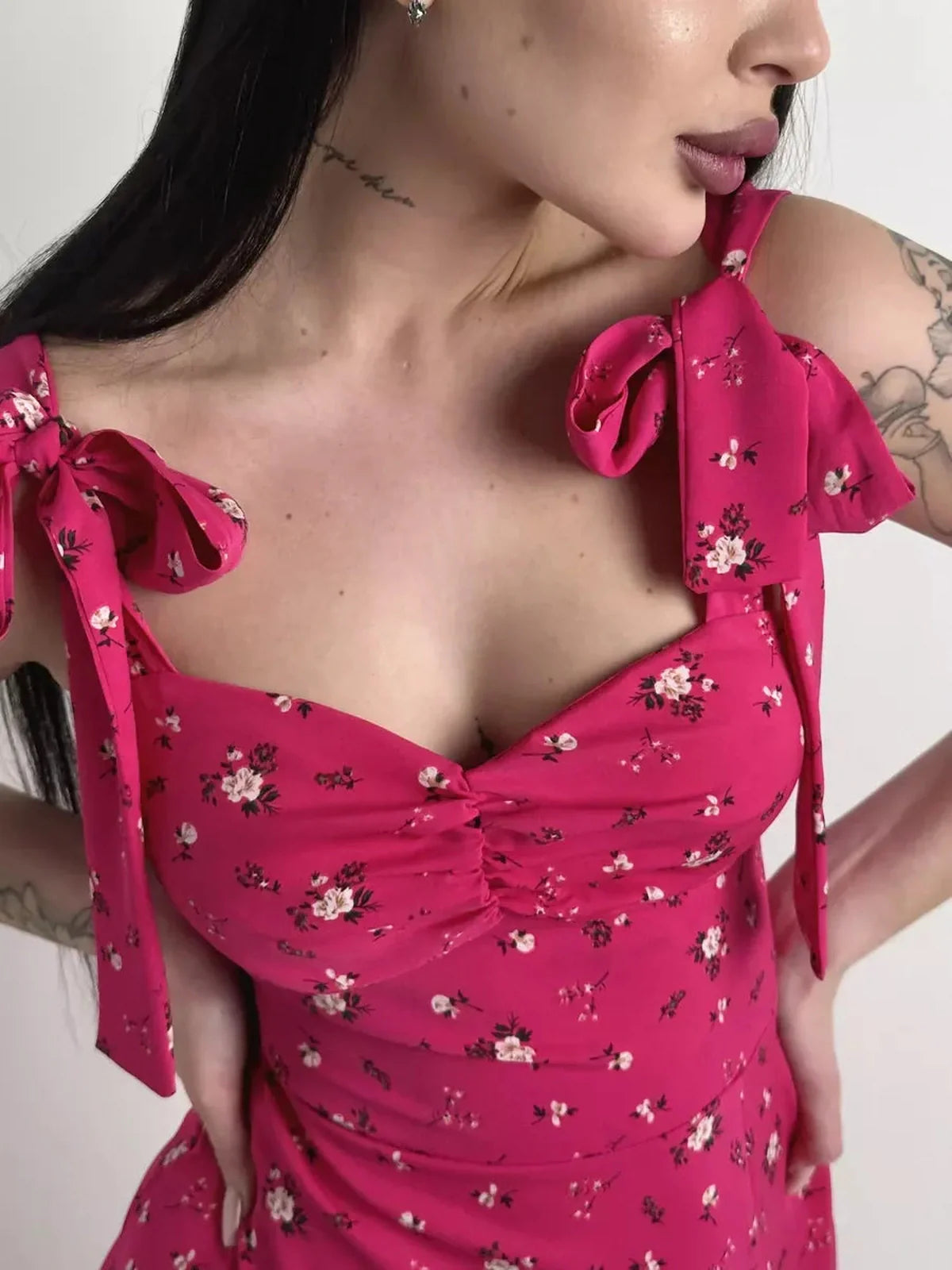 Close-up of a woman wearing a vibrant pink floral midi dress with sweetheart neckline and adjustable shoulder ties.