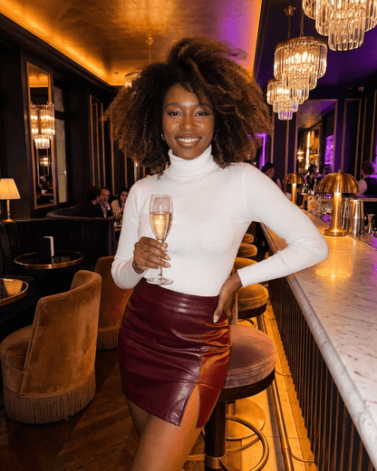 Bordeaux Mini Skirt styled with a chic white turtleneck, showcasing the smooth PU finish and front slit.