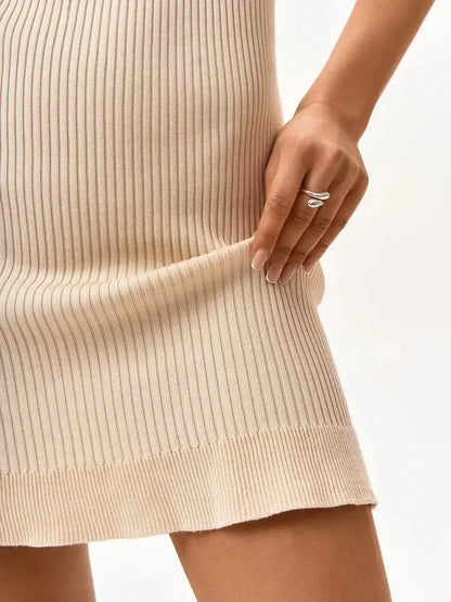 Close-up of a model holding the hem of a sleek beige ribbed mini dress, showcasing its texture and fit.