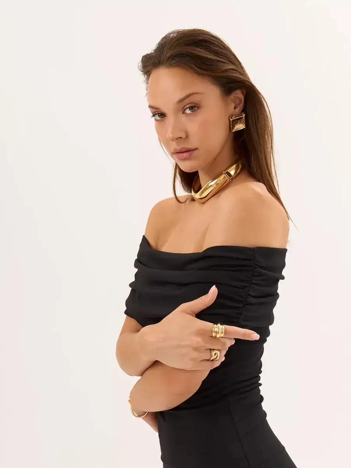 Glamorous woman wearing a black off-shoulder bodycon dress paired with bold gold jewelry.