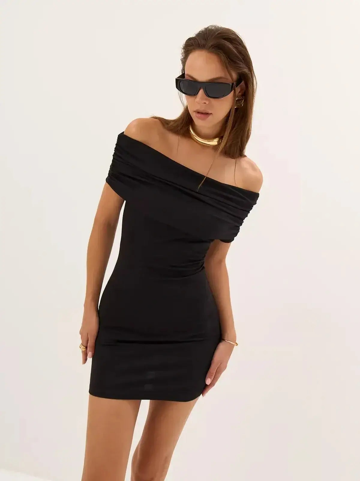 Stylish woman in a black bodycon mini dress with off-the-shoulder design and sunglasses, perfect for summer events.