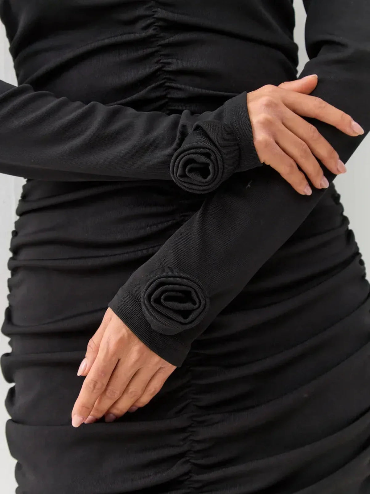 Close-up of long sleeves with gathered ruching on a black dress, showcasing elegant design details for formal occasions.