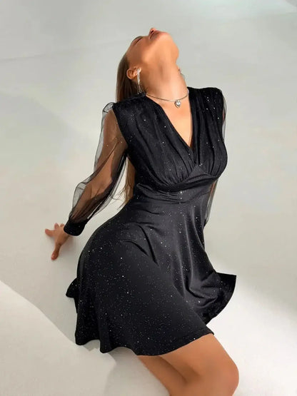 Elegant black mini dress with plunging neckline and sheer long sleeves, perfect for parties and formal occasions.