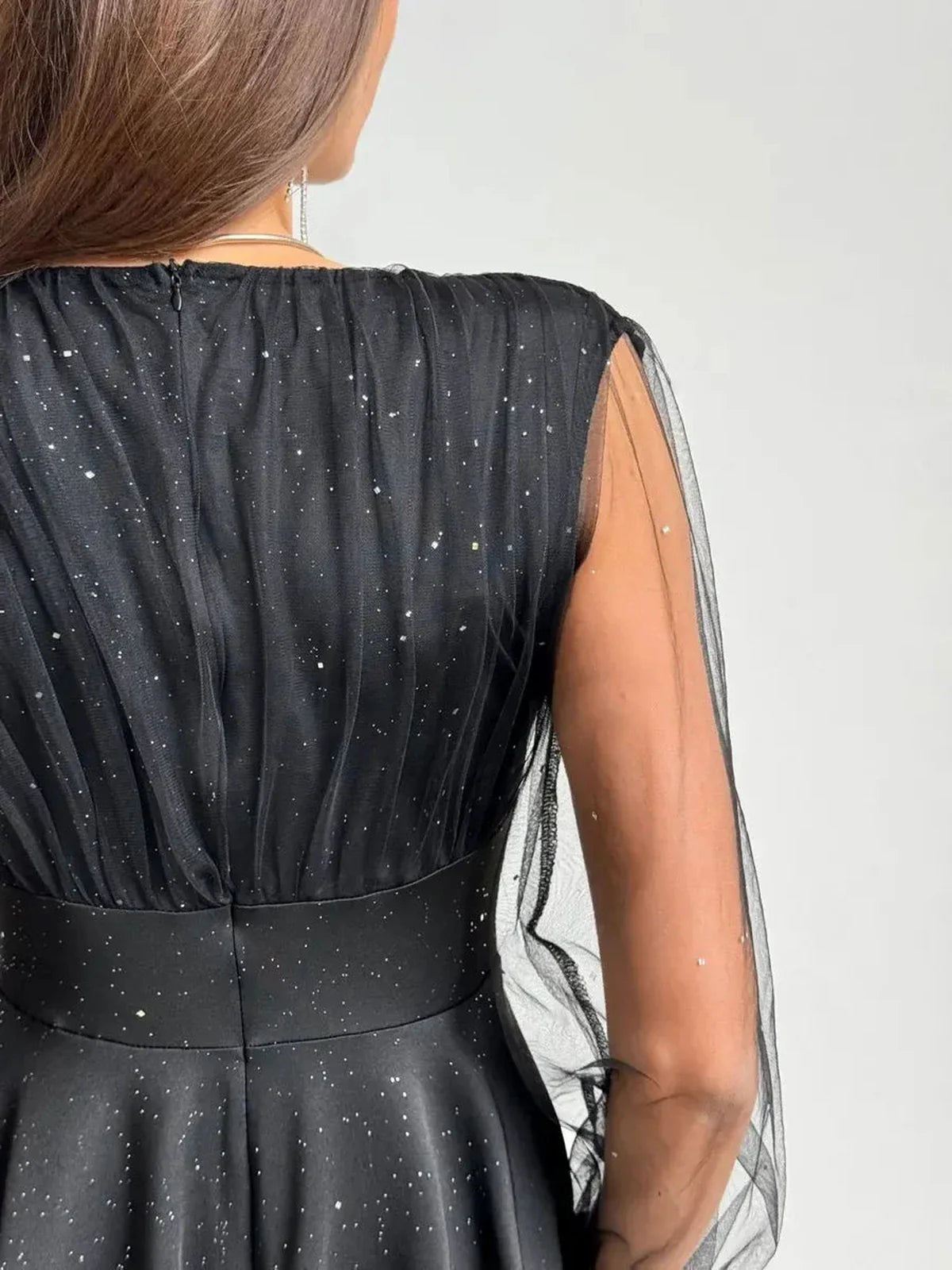 Back view of a black mini dress with shimmering fabric and sheer long sleeves, perfect for evening occasions.