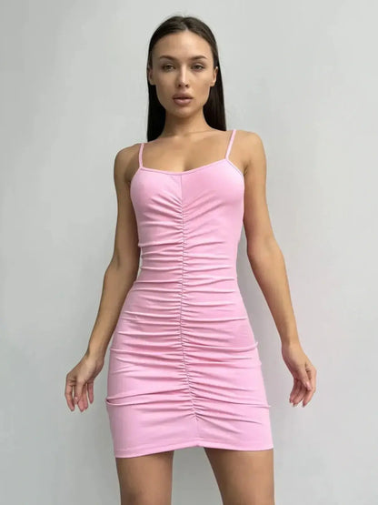 Model wearing a pink bodycon mini dress with spaghetti straps and flattering ruching in front.