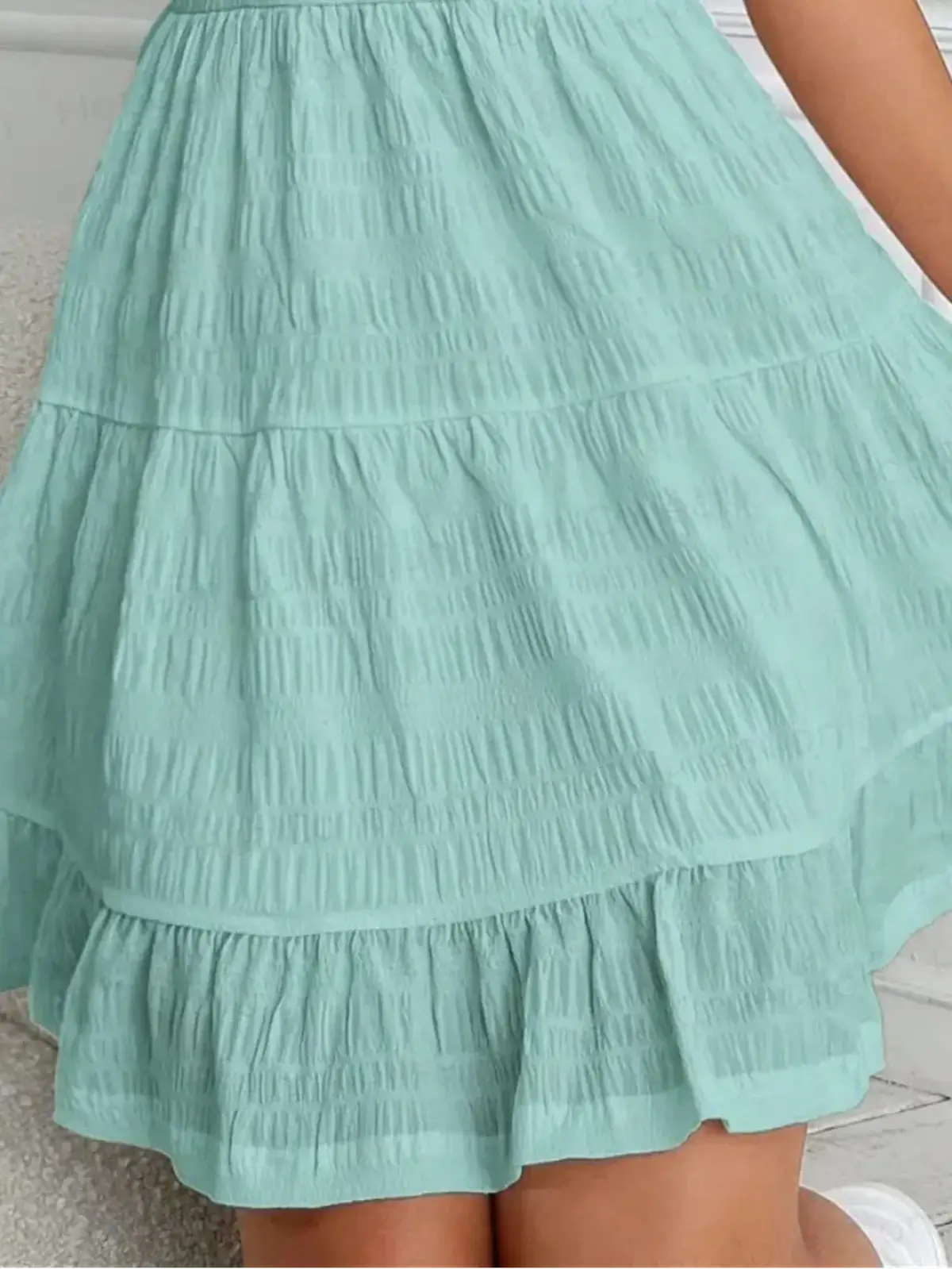 Close-up of the cascading tiered skirt of a soft mint Breeze Tier Mini Dress for summer occasions.