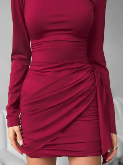 Burgundy Grace mini dress featuring long sleeves, draped ruching, and an elegantly tied waist sash for a flattering fit.