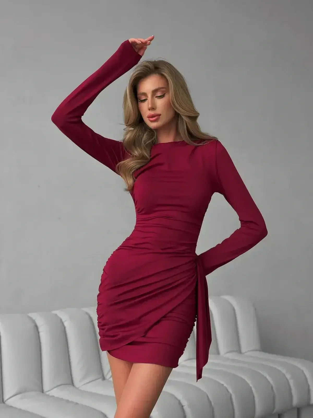 Burgundy Grace mini dress featuring long sleeves, ruched detailing, and a tied waist for an elegant and flattering fit.