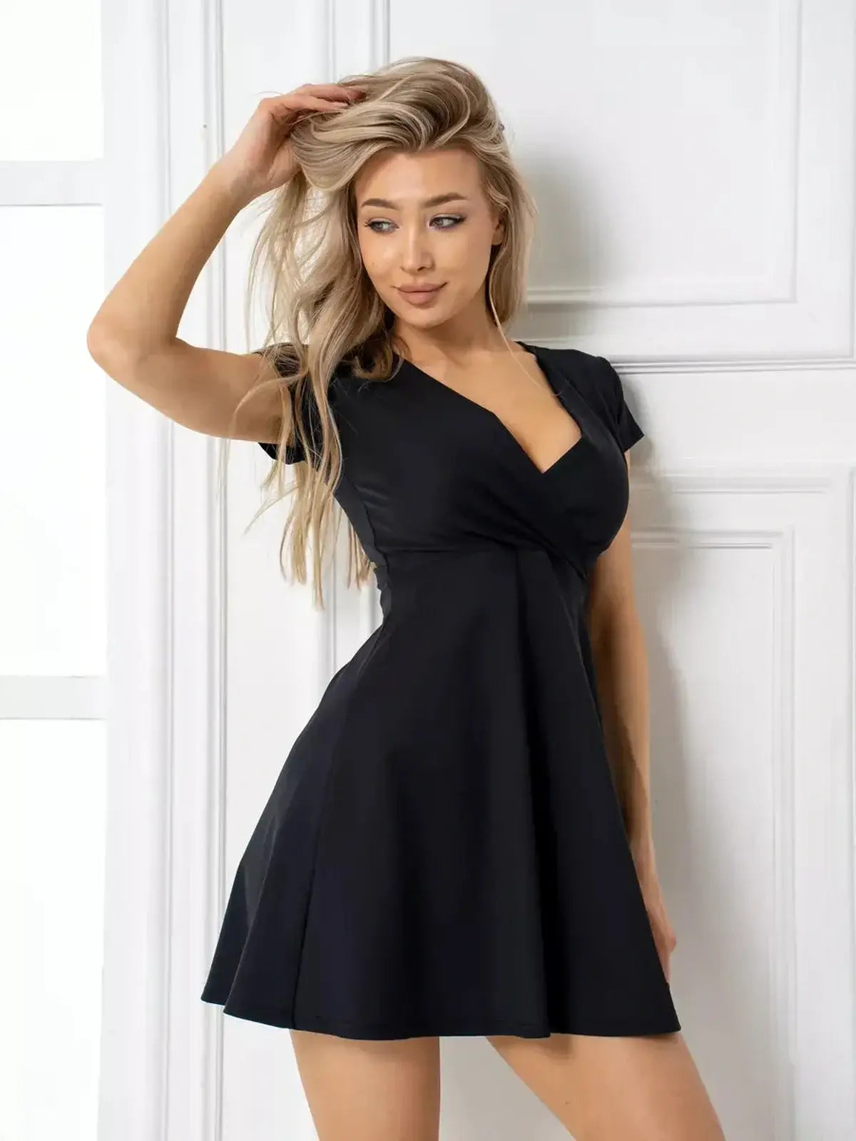 Model wearing the Charm Curve Mini Dress, a chic black dress with a V-neckline and flared skirt, perfect for summer or cocktail events.