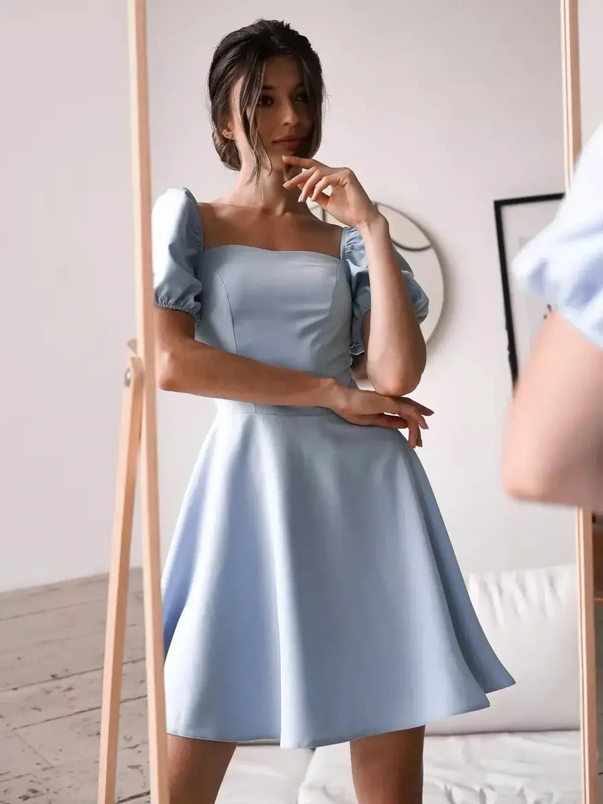 Model wearing a light blue mini dress with puff sleeves, displayed in front of a mirror, showcasing elegant style.