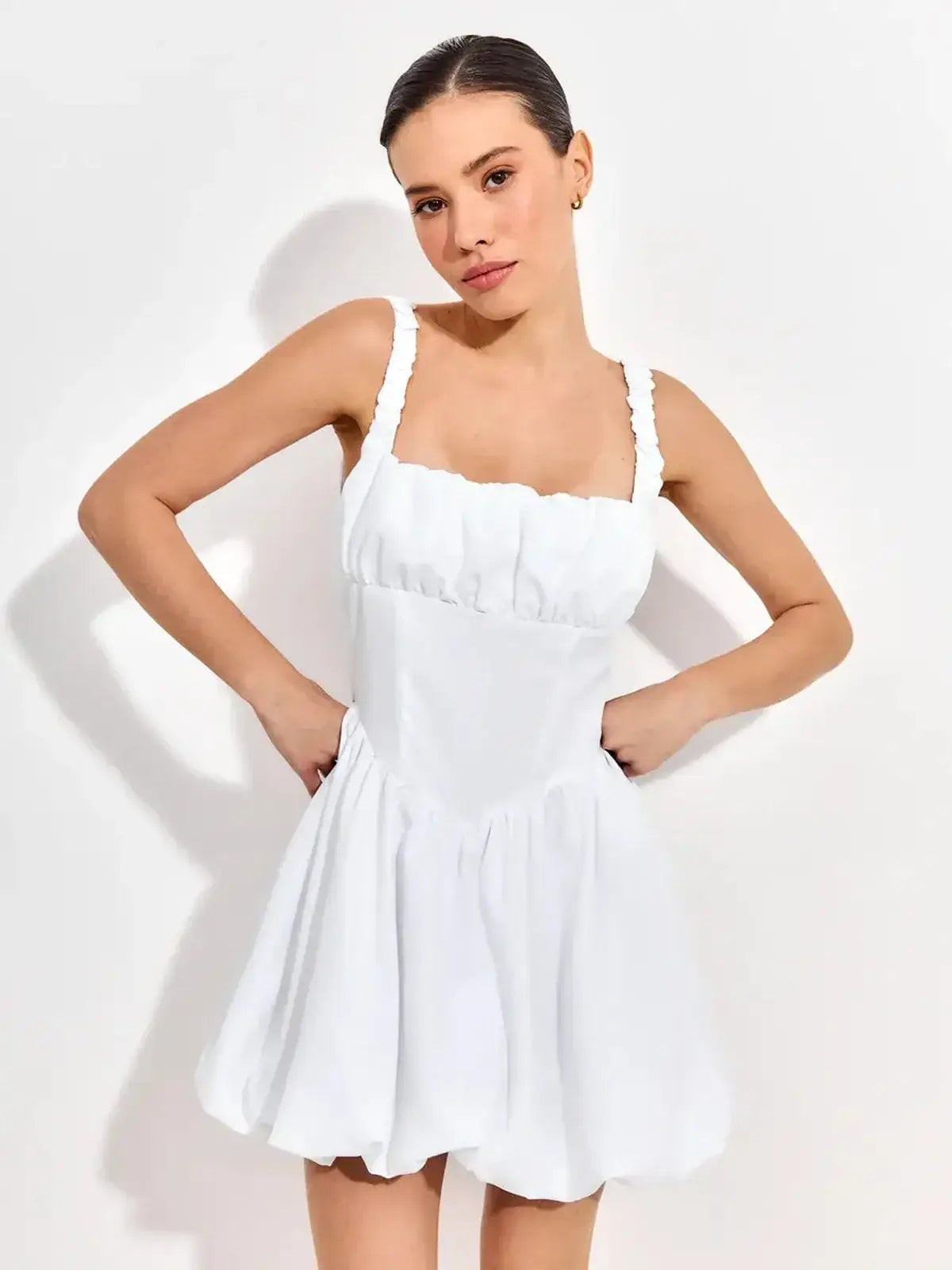 Model wearing a whimsical white mini dress with ruffled straps and a sculpted bodice, ideal for summer celebrations.