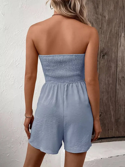 Back view of a woman wearing a light blue strapless mini dress with a smocked bodice and relaxed fit.