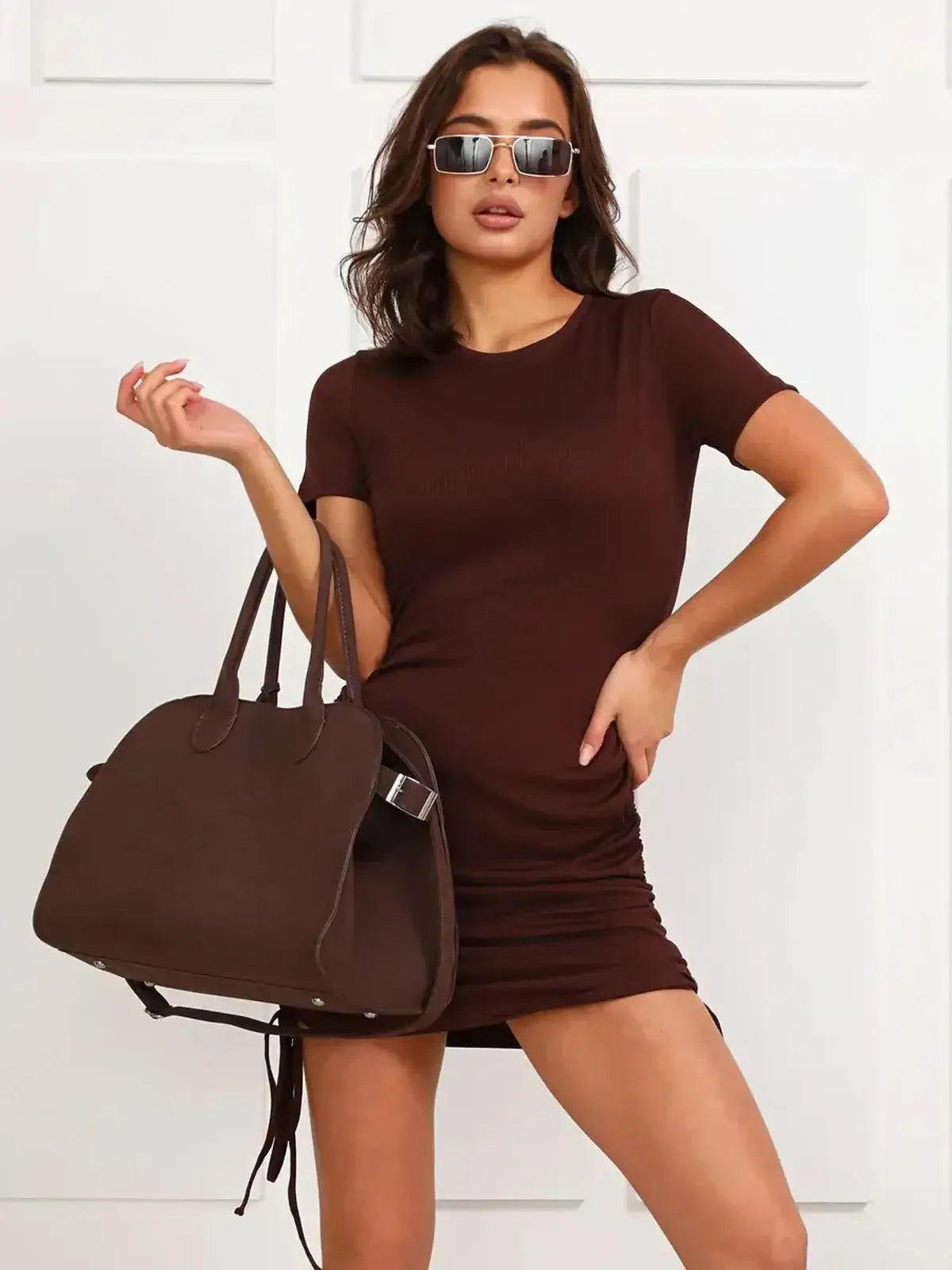 Cocoa Cinch bodycon mini dress in chocolate brown, styled with sunglasses and a stylish handbag.
