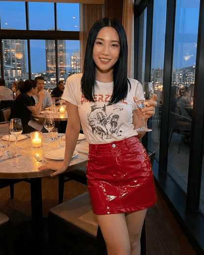 Woman in a restaurant wearing a Crimson Mini Skirt by Slimona, holding a drink, with city skyline in the background.