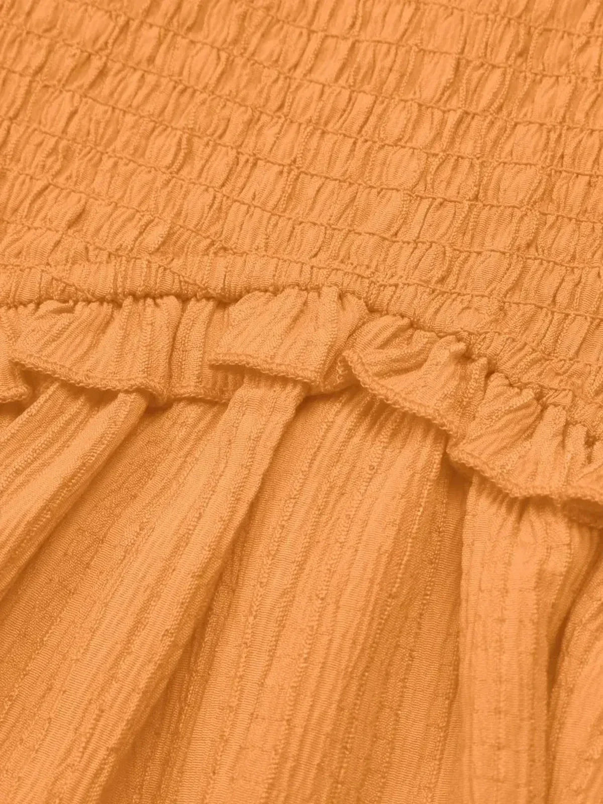 Close-up of the textured smocked bodice and ruffle detailing of the Eden Tier Mini Dress in orange.