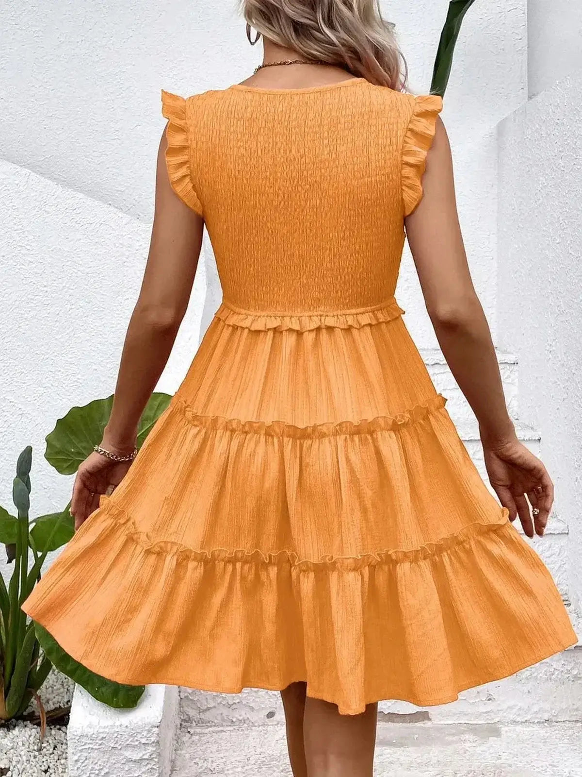 Back view of a model wearing the Eden Tier Mini Dress in orange, showcasing its ruffle detailing and flowing silhouette.