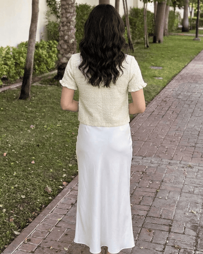 Elara Cardigan by Slimona, viewed from behind, showcasing the short sleeve design with white skirt in an outdoor setting.