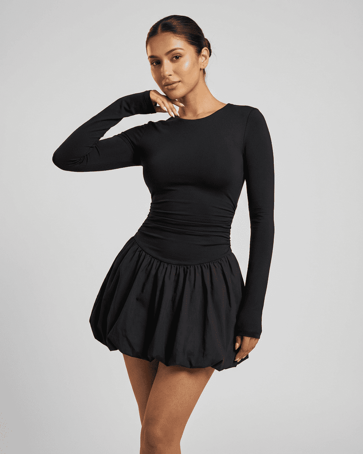 Model wearing Slimona Elara Mini Dress, a fitted stretchy elegant long sleeve tiered mini dress in black.