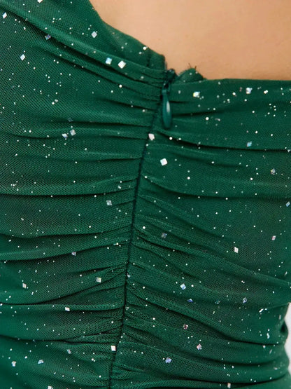 Close-up of emerald green dress with ruched detailing and silver sparkle accents, perfect for summer and evening occasions.