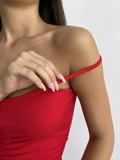 Close-up of a woman adjusting the spaghetti strap of a red mini dress, showcasing its curve-enhancing design.