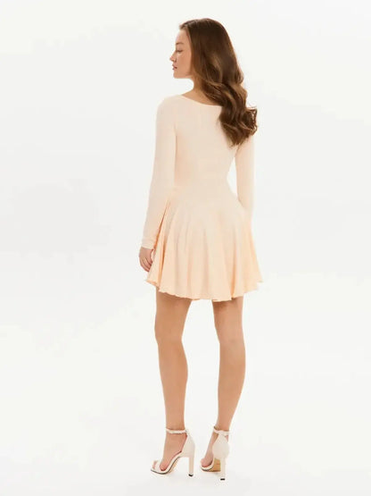 Back view of a woman in a flared long sleeve peach mini dress, perfect for summer parties or wedding guest attire.