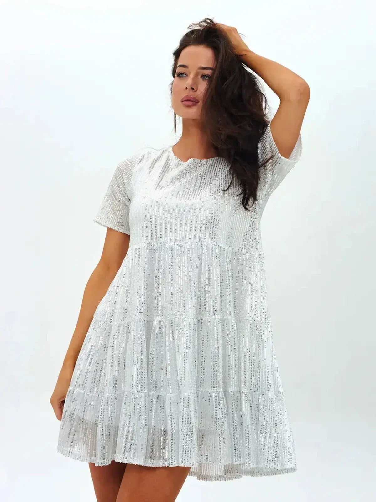 Model wearing a dazzling white sequin mini dress with a flowing silhouette and tiered hem.