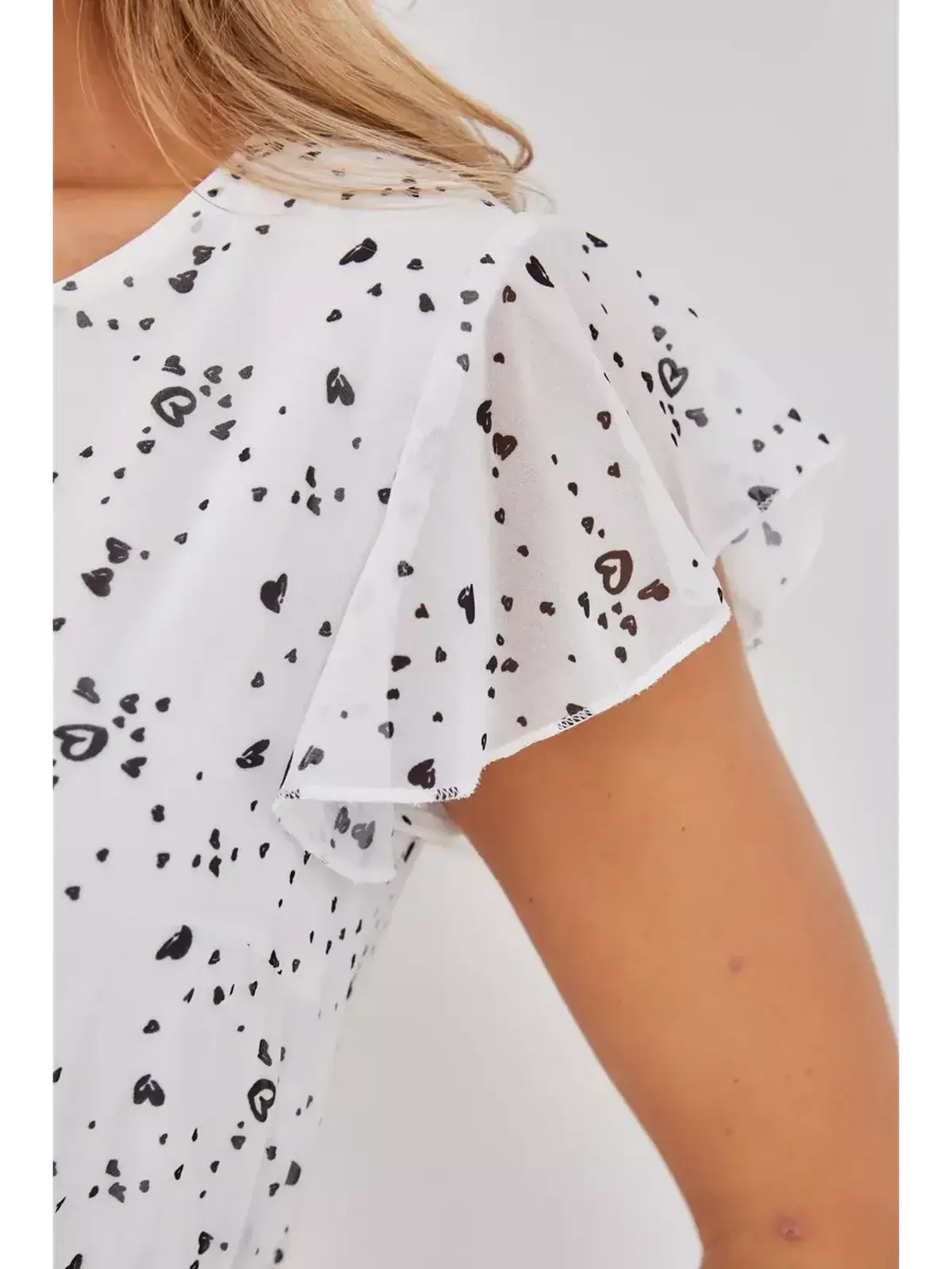 Close-up of flutter sleeve on a white mini dress with black heart prints, perfect for summer celebrations.