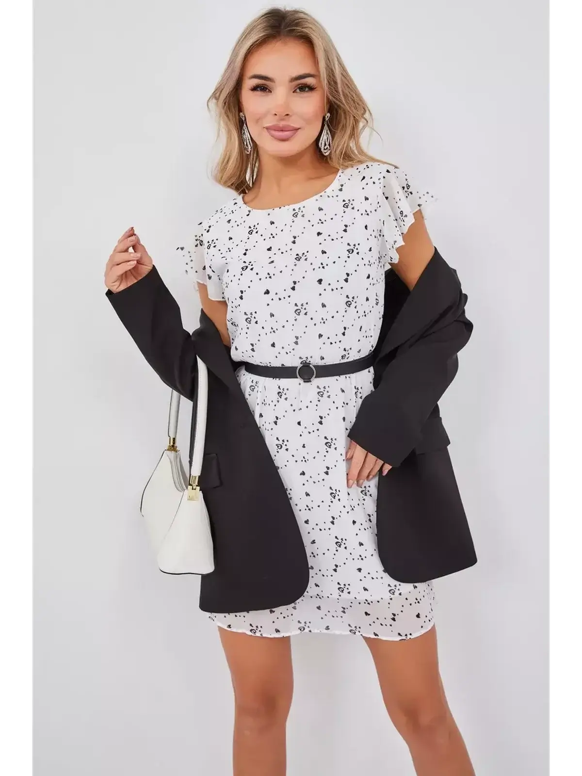 Model wearing the Heartline Charm white mini dress with black hearts, styled with a blazer and accessories.