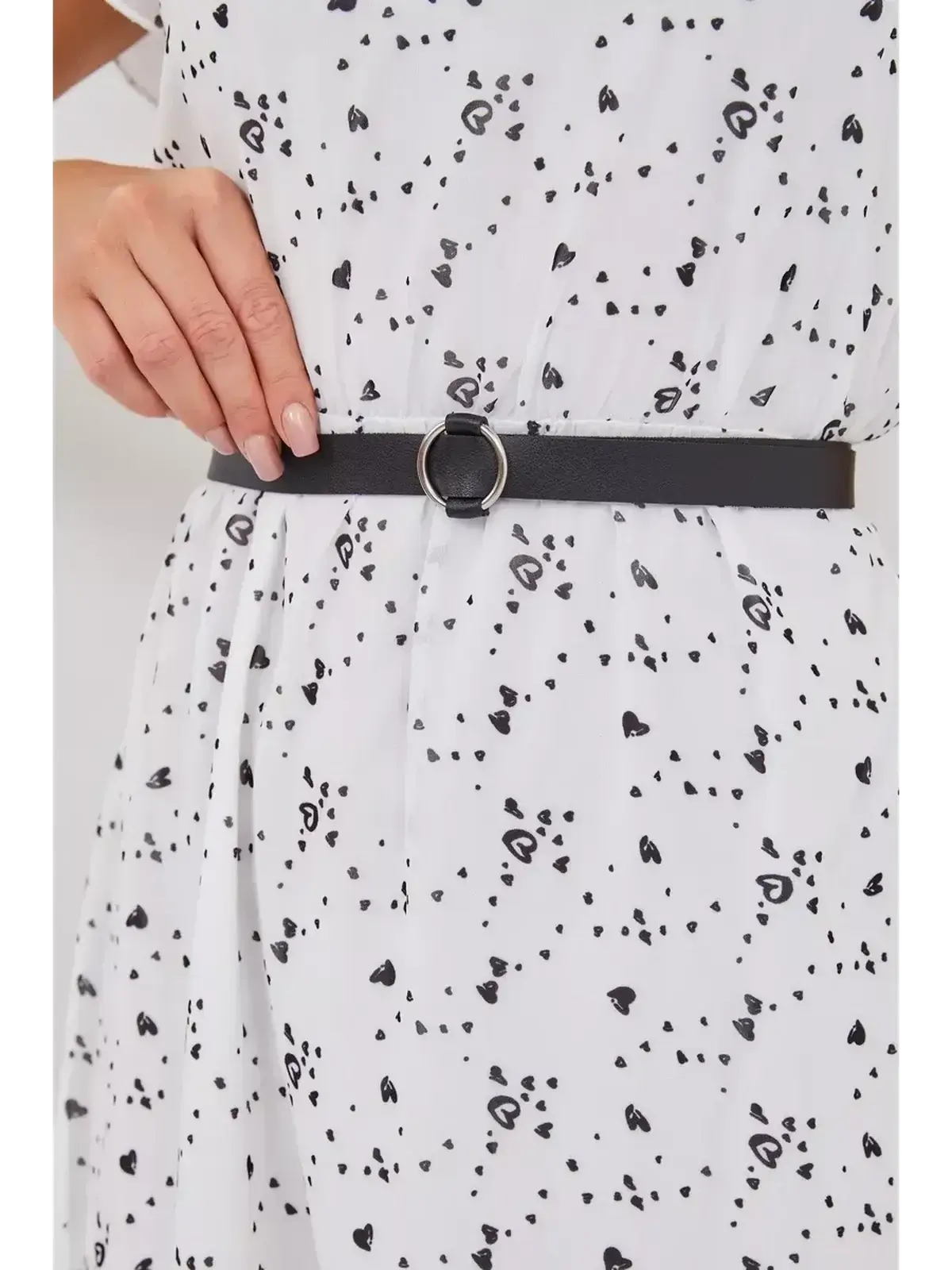 Close-up of black belt cinched at the waist of a white dress with scattered black hearts, showcasing stylish details.