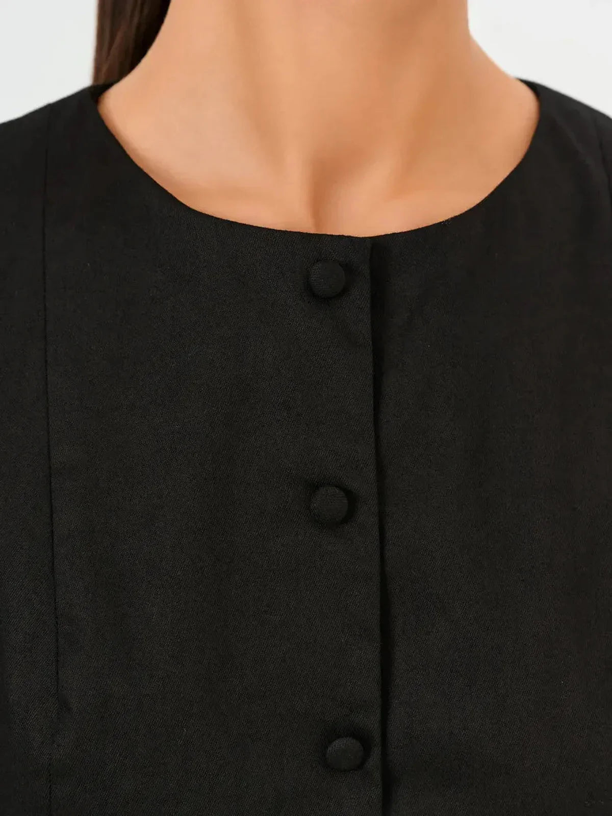 Close-up of the round neckline and button detail on a sleek black mini dress.