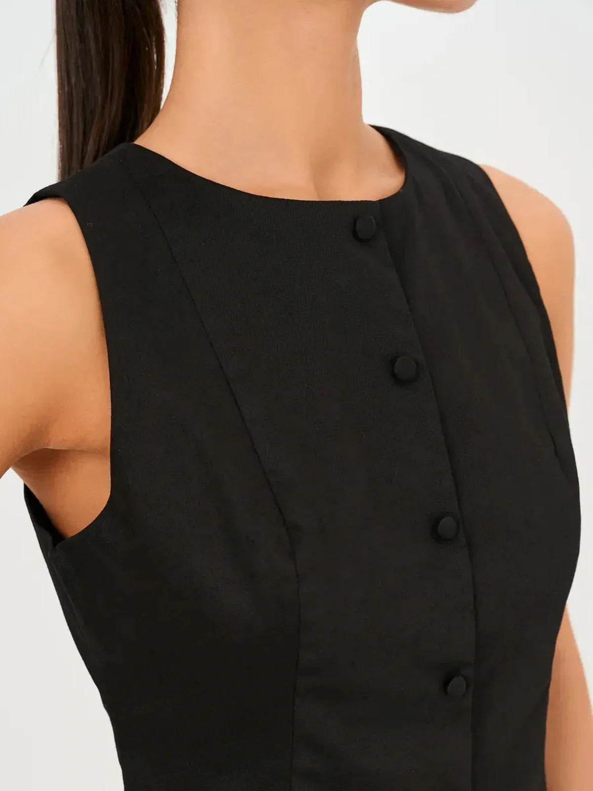 Close-up of a sleeveless black dress featuring a round neckline and architectural button detail.