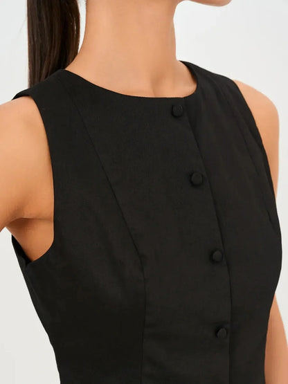 Close-up of a sleeveless black dress featuring a round neckline and architectural button detail.