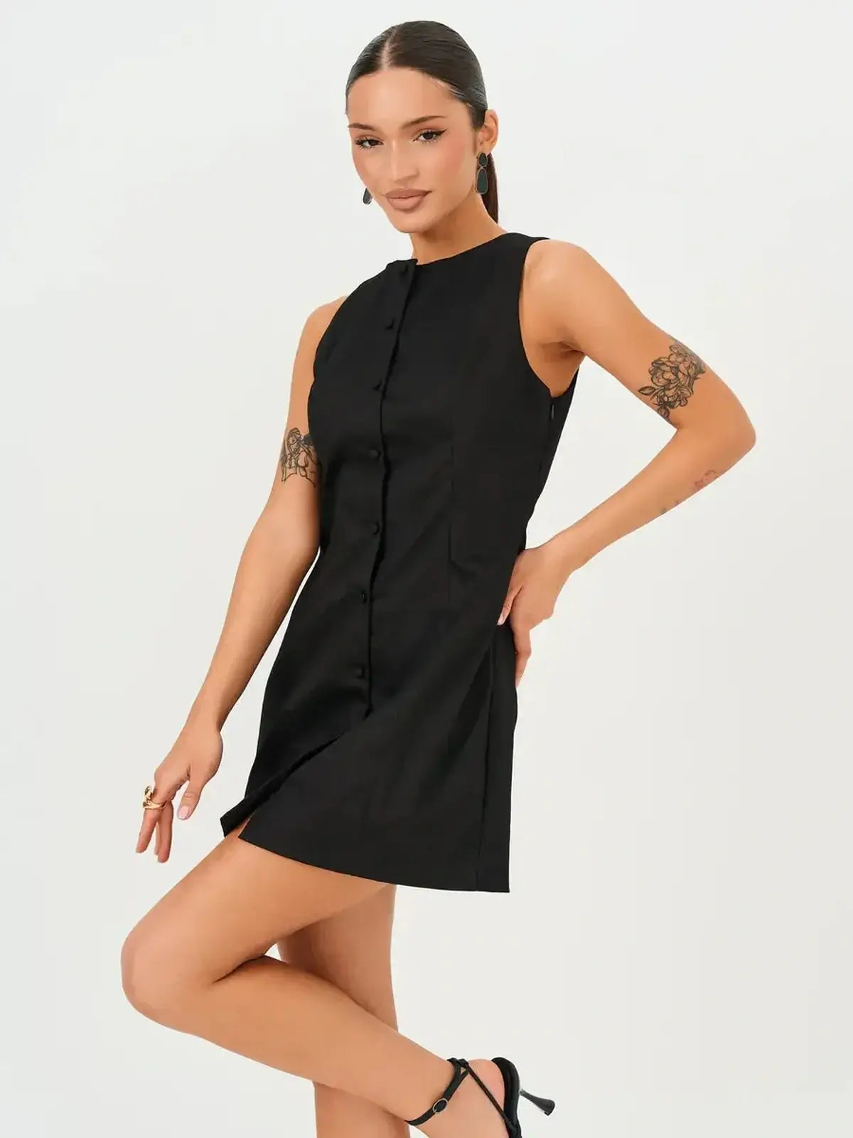 Model showcasing the Icon Edge Mini Dress, a stylish black dress with a sleeveless design and architectural button detail.