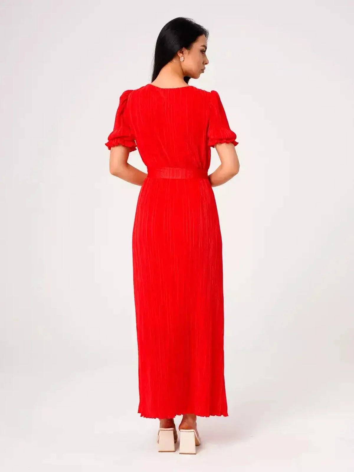 Back view of a woman wearing a red pleated maxi dress, showcasing puff sleeves and a belted waist.