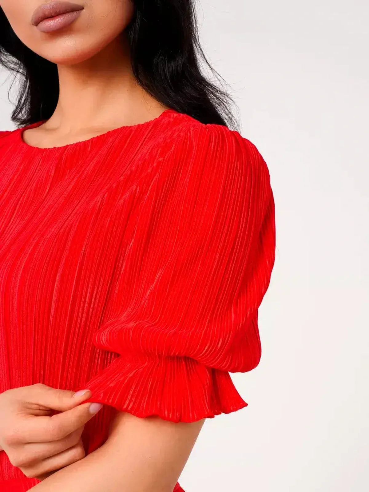 Close-up of a woman's hand on a red pleated dress with puff sleeves, highlighting its elegant design.