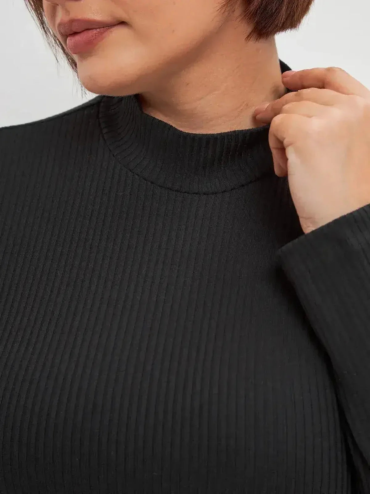 Close-up of a woman's neckline in a black ribbed midi dress, highlighting its elegant texture and design.