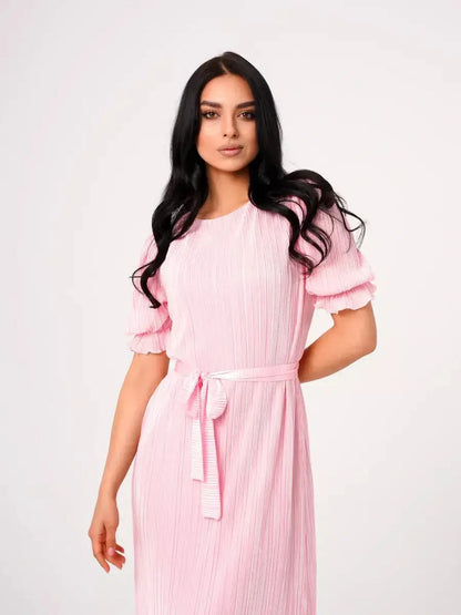 Model wearing the Celeste Maxi Dress, a pink pleated dress with puff sleeves and a tie waist, perfect for summer events.