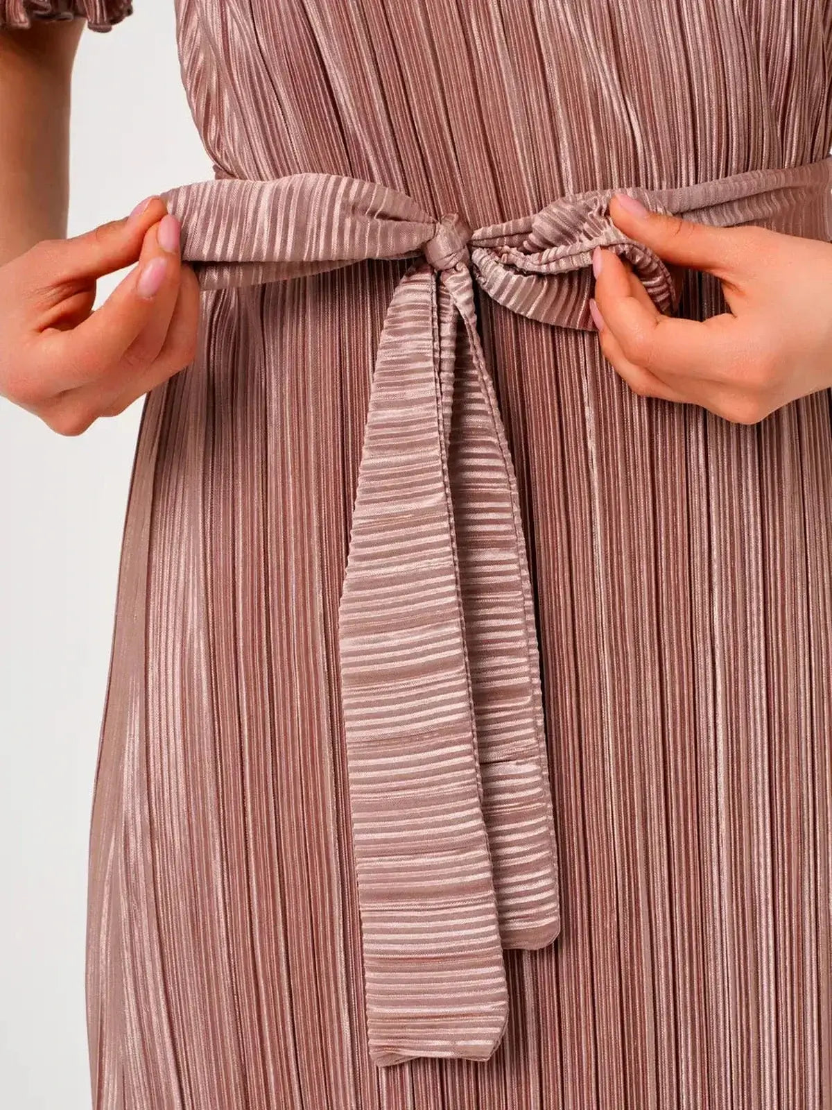 Close-up of a model tying the waist belt on the light cappuccino-hued Celeste Maxi Dress with elegant pleats.