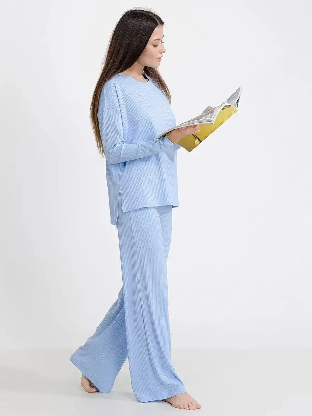 Woman in light blue ribbed knit lounge set, reading a magazine for relaxed comfort and style.