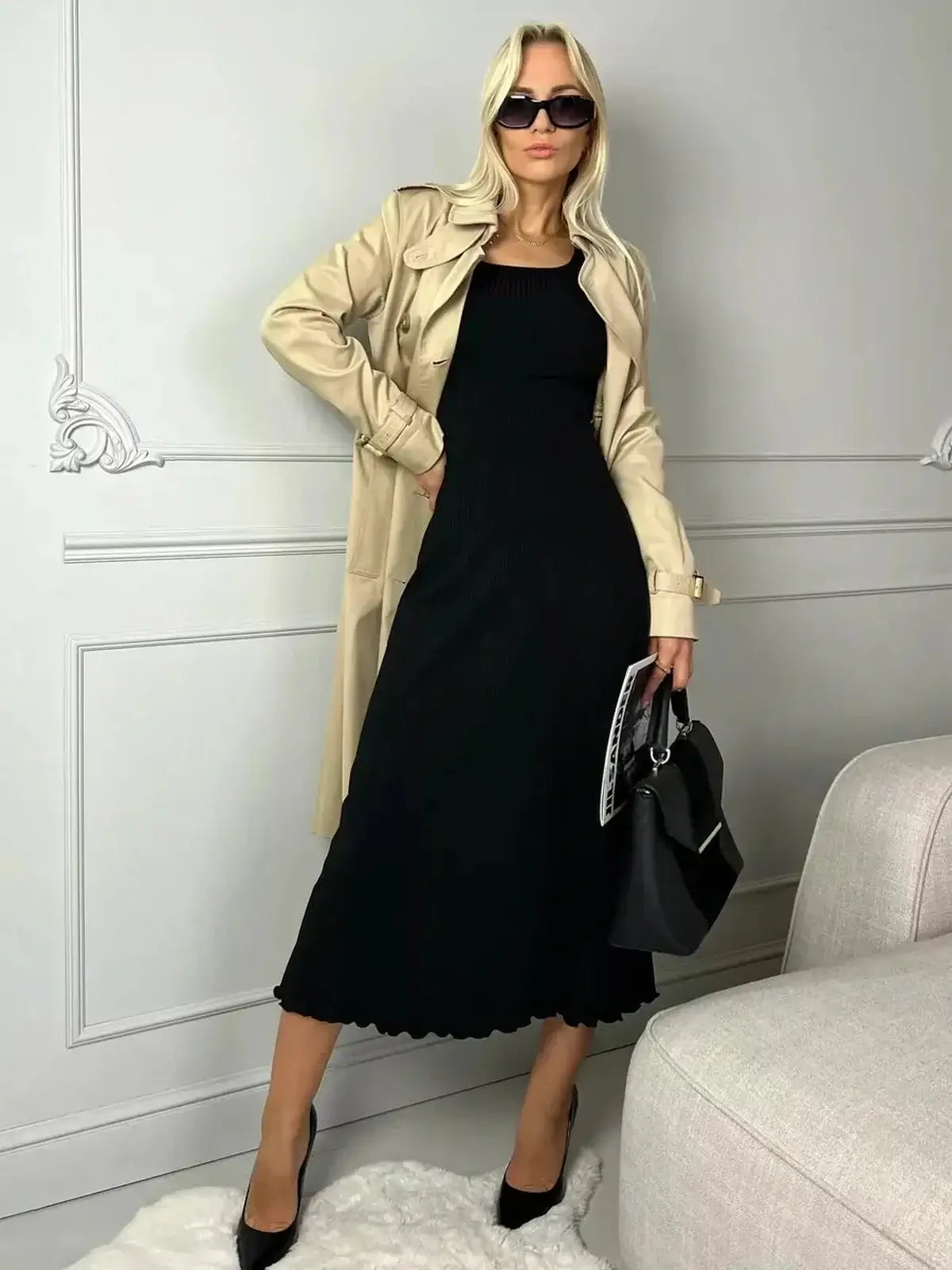 Stylish woman in a black midi dress paired with a trench coat and sunglasses, perfect for chic outings.