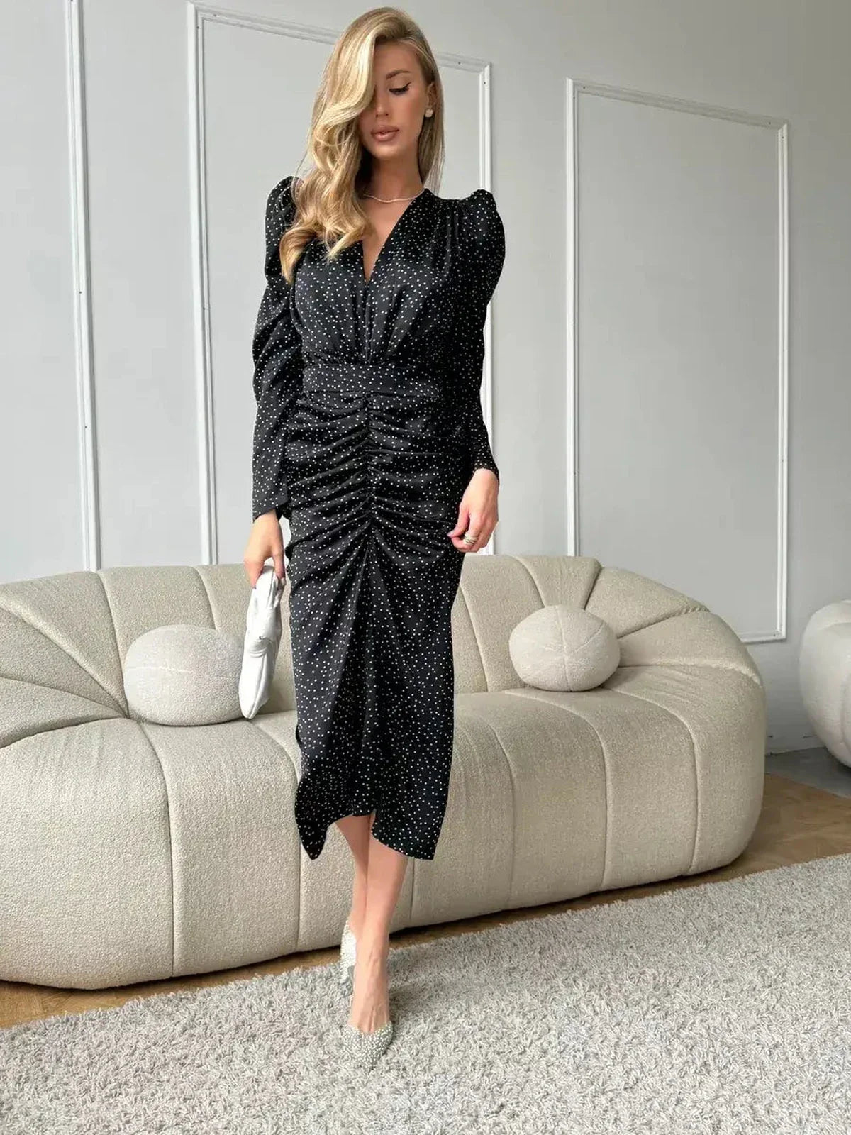 Model showcasing the Velina Midi Dress with elegant draping, black with white polka dots, perfect for cocktails or weddings.