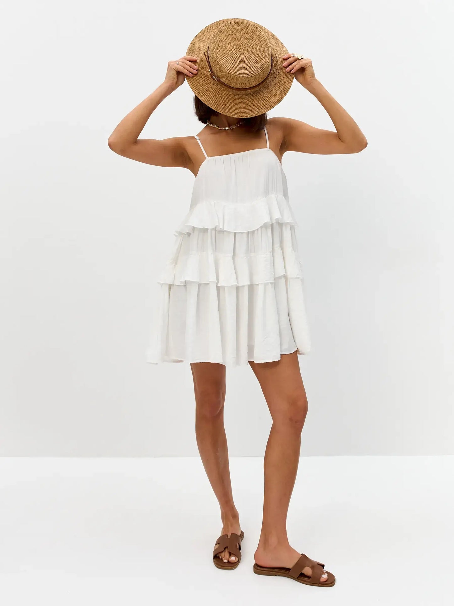 Model wearing a lightweight white summer dress with ruffles and a straw hat, perfect for weddings or casual outings.