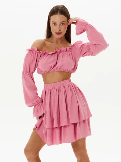 Feminine tiered ruffle set featuring an off-shoulder crop top and layered mini skirt in pink, perfect for summer and special occasions.