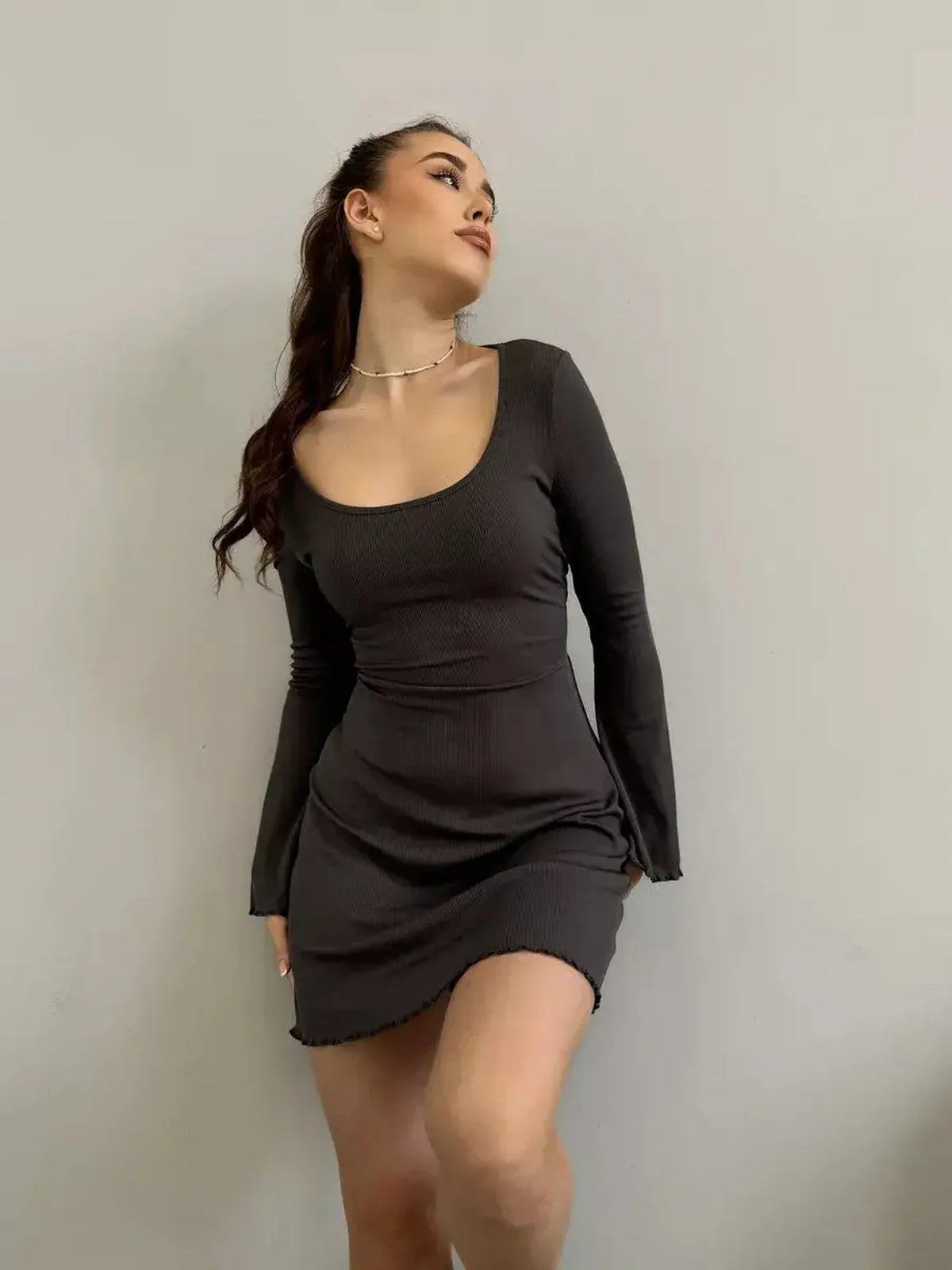 Model showcasing the Noir Flare black mini dress with a deep square neckline and flared long sleeves.