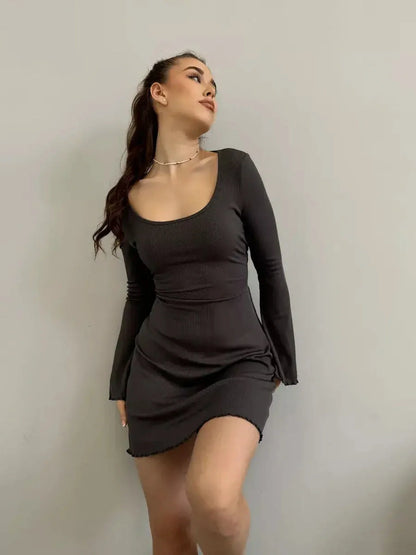 Model showcasing the Noir Flare black mini dress with a deep square neckline and flared long sleeves.