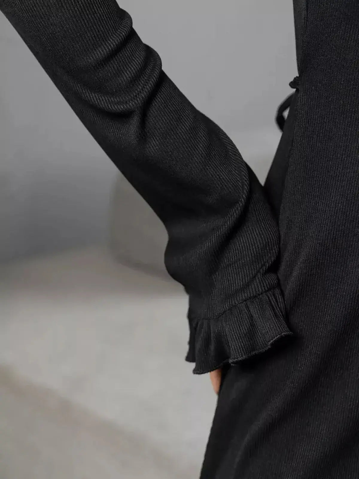 Close-up of a black dress sleeve featuring a ribbed texture and ruffled trim, showcasing elegant design details.