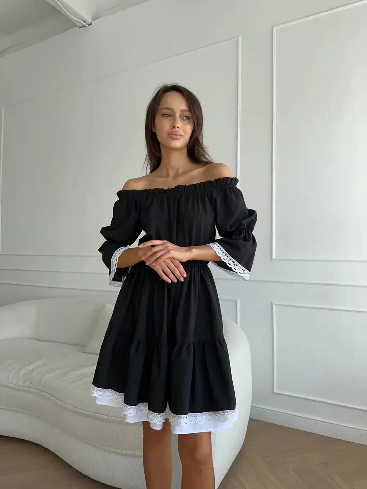Model showcasing a black off-shoulder mini dress with tiered ruffles and white lace trim, perfect for weddings or special occasions.
