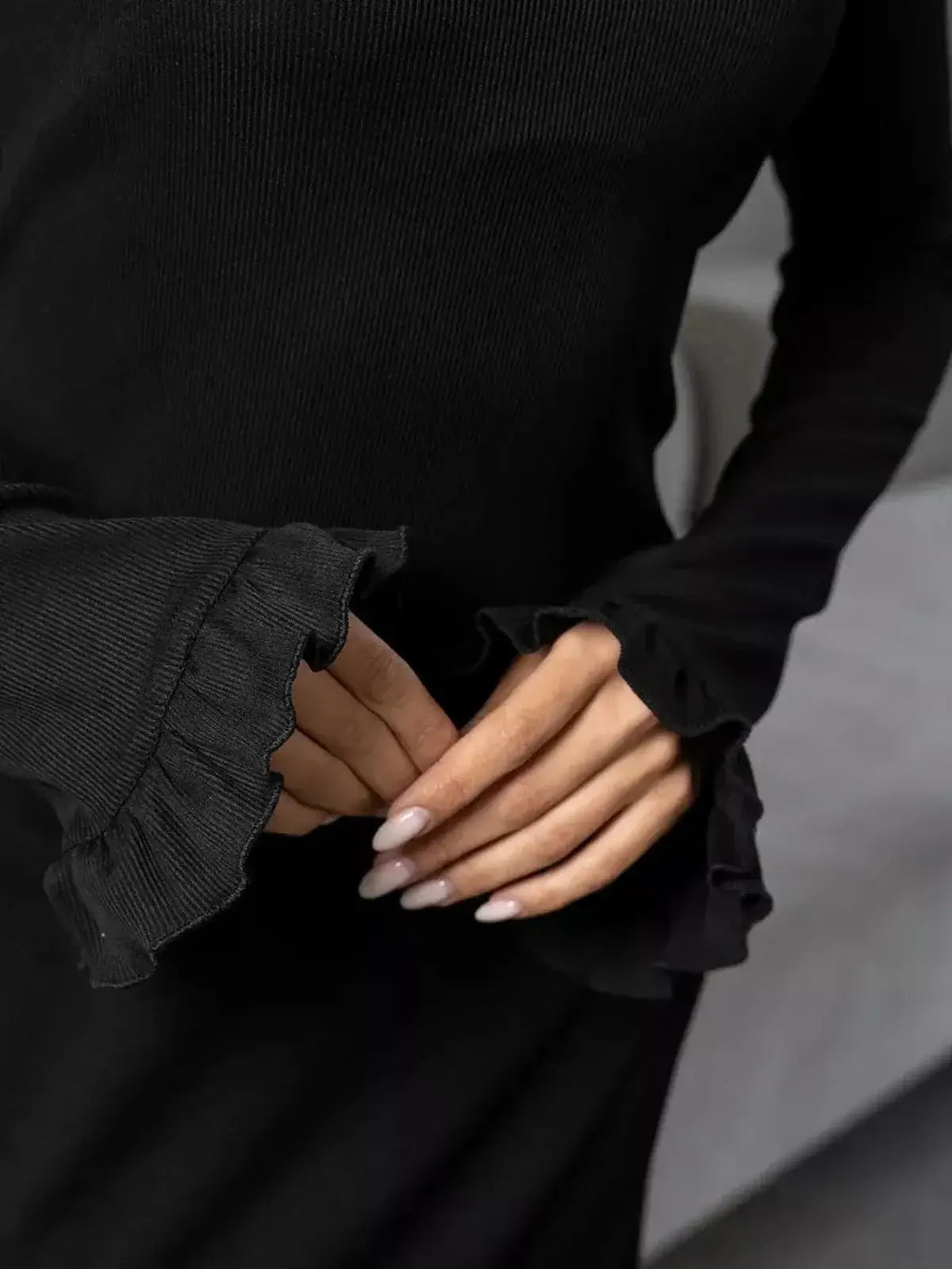 Close-up of a woman in a black ribbed dress showcasing ruffled sleeves for a chic look.