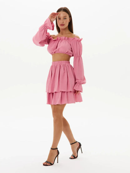 Woman in a pink off-shoulder crop top and tiered mini skirt, showcasing playful elegance for summer events or weddings.